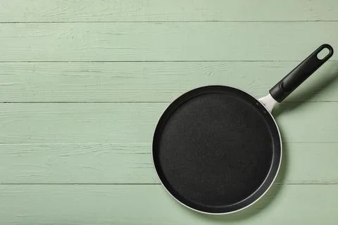 Empty black non-stick frying pan with handle on light green wooden table, kit Stock Photos
