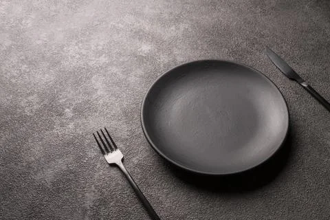 Empty black plate, fork and knife on a dark background, horizontal photo Stock Photos
