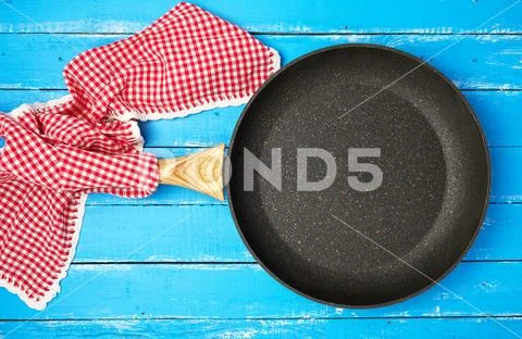 Empty black round frying pan with wooden handle and red kitchen napkin Stock Photos