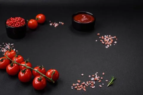 Empty black texture table, cherry tomatoes on a twig, spices, salt and herbs Stock Photos