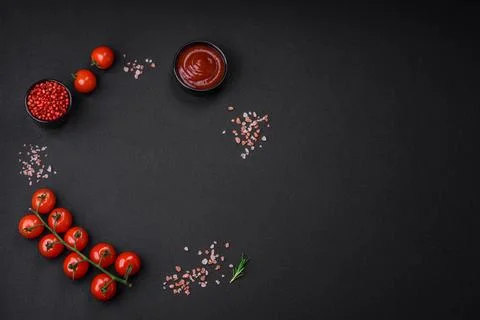 Empty black texture table, cherry tomatoes on a twig, spices, salt and herbs Stock Photos