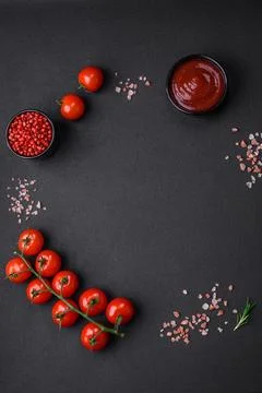 Empty black texture table, cherry tomatoes on a twig, spices, salt and herbs Stock Photos