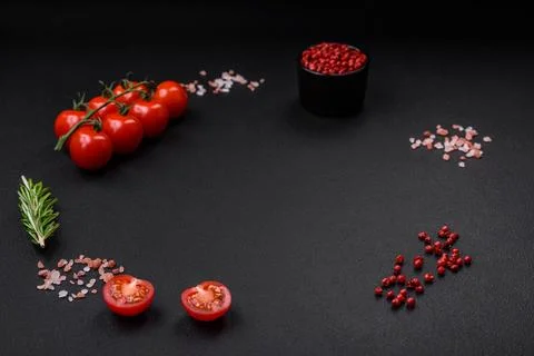 Empty black texture table, cherry tomatoes on a twig, spices, salt and herbs Stock Photos