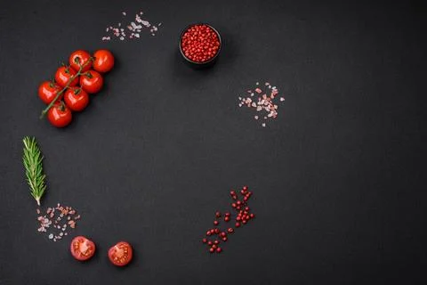 Empty black texture table, cherry tomatoes on a twig, spices, salt and herbs Stock Photos