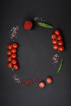 Empty black texture table, cherry tomatoes on a twig, spices, salt and herbs Stock Photos