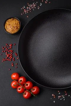 Empty black texture table, cherry tomatoes on a twig, spices, salt and herbs Stock Photos