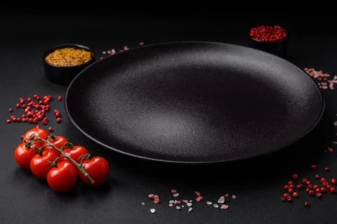 Empty black texture table, cherry tomatoes on a twig, spices, salt and herbs Stock Photos