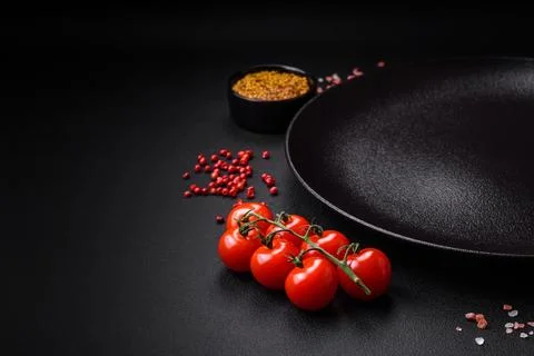 Empty black texture table, cherry tomatoes on a twig, spices, salt and herbs Stock Photos