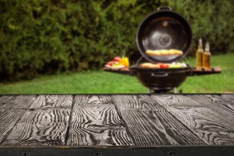 Empty black wooden table and blurred view of tasty food on modern barbecue gr Stock Photos