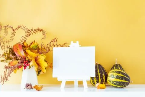Empty blank canvas on a stand, decorative striped pumpkins, vase with bouquet Foto stock