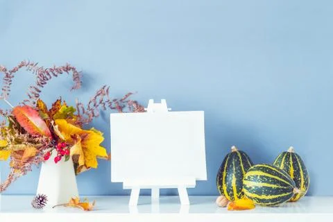 Empty blank canvas on a stand, decorative striped pumpkins, vase with bouquet Stock Photos