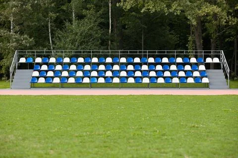 Empty blue and white seats in a footbal or soccer stadium. Grass field and pl Stock Photos