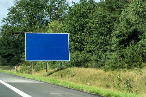 Empty blue billboard standing on the grass verge beside a highway with dense Stock Photos