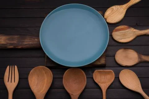 Empty blue ceramic plate on an old wooden cutting board with spoon and fork a Stock Photos