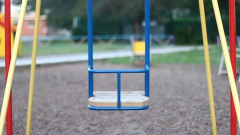 Empty blue children's swing swinging in the wind during the day at the playgr Видео 131955769