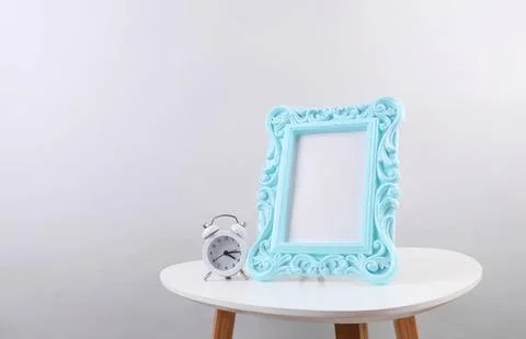 Empty blue decorative frame and alarm clock on white table Stock Photos