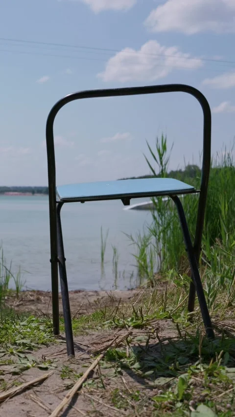 Empty Blue Folding Chair Standing by a Calm Lake Shore Outdoors Video stock 342767737