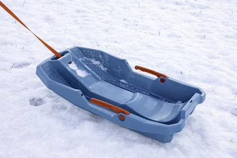 Empty blue plastic sled with a red rope lies on a snow-covered ground.space for Stock Photos