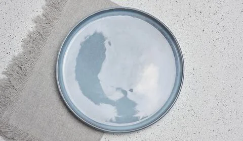 Empty blue plate with golden edging next to grey linen napkin on mottled wh.. Stock Photos