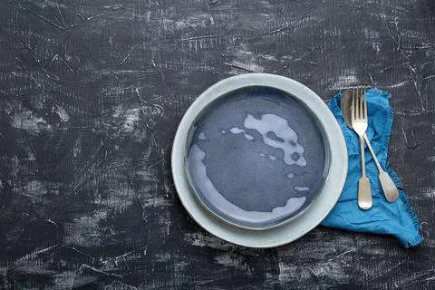Empty blue plate served with fork spoon table napkin. Dark black concrete tab Stock Photos