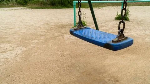 Empty Blue Playground Swing Seat on a Sandy Park Ground 写真素材