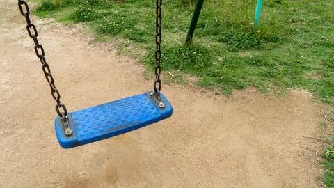 Empty Blue Swing Seat Hanging Over Sandy Park Playground Ground 写真素材