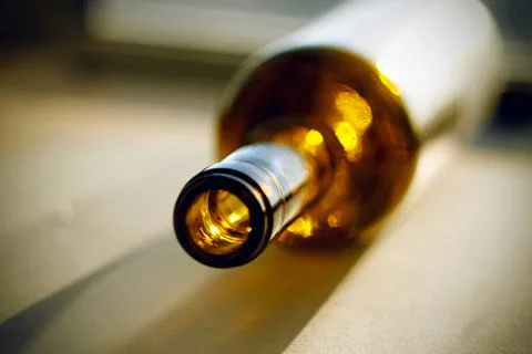 An empty bottle of strong alcohol, left after drinking, lies on the sunlit su Stock Photos