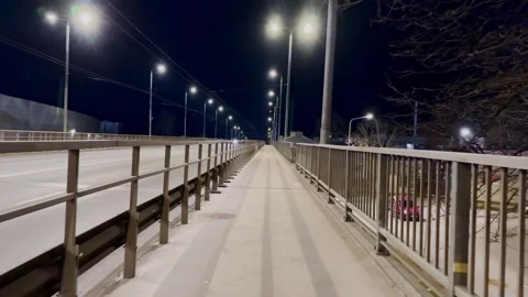 Empty bridge sidewalk at night with bright streetlights, metal railings, road Stock Footage 336237116