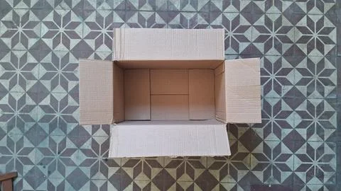 Empty brown cardboard box sitting on a vintage patterned floor Stock Photos