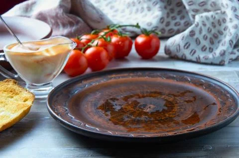 Empty brown clay plate on the table with a gravy boat, cherry tomatoes, bread Stock Photos
