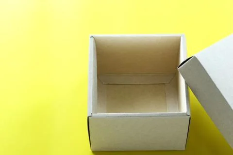 Empty brown paper box rests on a yellow paper floor and have copy space. Stock Photos