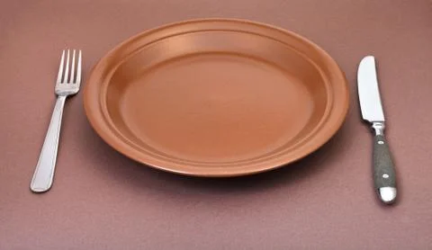 Empty brown plate with fork and knife set on brown Stock Photos