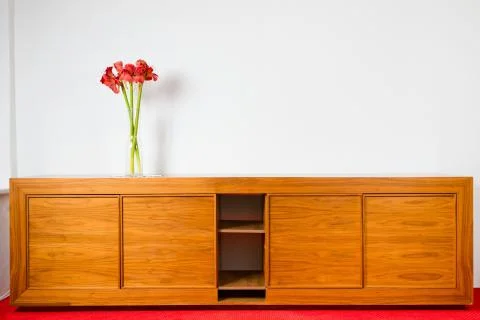 Empty brown wooden commode with three flowers on red car carped and next to w Foto stock