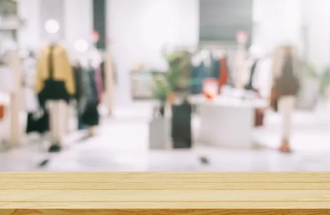 Empty brown wooden table and De focused/blurry background of clothing store.. Stock Photos