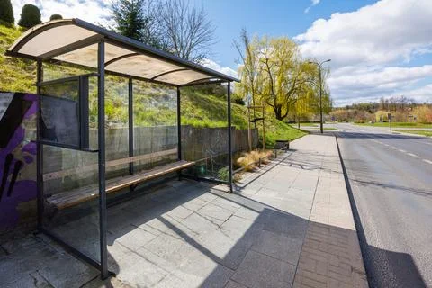 An empty bus stop on the side of the road on a spring day. Covered bus stop. Stock Photos