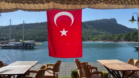 Empty cafe on sea beach with red Turkish flag and boat on water, hill and for Stock Footage 222704552