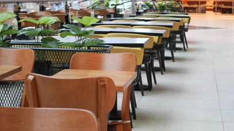 Empty cafe seating with wooden tables and chairs in row, person walking by. Stock Footage 333155737