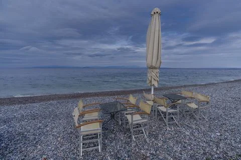 Empty cafe tables and folded umbrellas on the pebbled seashore Stock Photos
