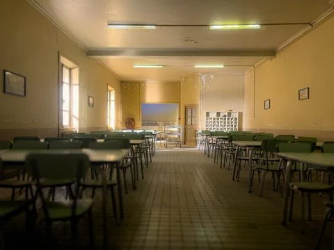 An empty cafeteria with rows of tables and chairs, bathed in soft sunlight Stock Photos