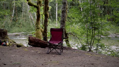 Empty Camping Chair by River in Peaceful Forest Setting | 4K Wilderness Scene Stock Footage 312084073