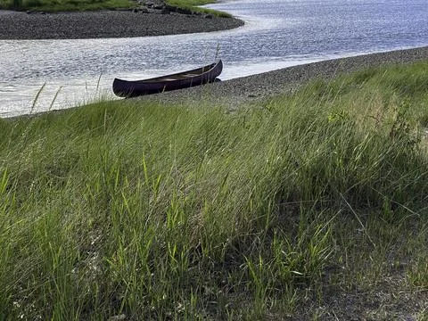 Empty canoe sits at the edge of river Stock Photos