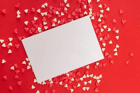 Empty card and small heart shaped sprinkles on red background Stock Photos