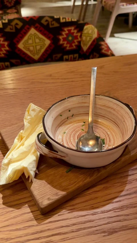 Empty Ceramic Bowl With Spoon, Creamy Broth Traces And Crumpled Napkin On Wooden Stock Footage 325231731