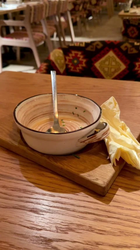 Empty Ceramic Bowl With Spoon, Creamy Broth Traces And Crumpled Napkin On Wooden Stock Footage 325231860