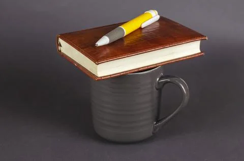 Empty ceramic mug, pen and notebook on gray background. New dark gray mug, ye Stock Photos