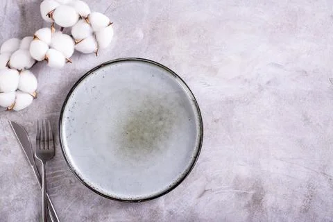 Empty ceramic plate, cutlery and cotton branch on gray background top view Stock Photos