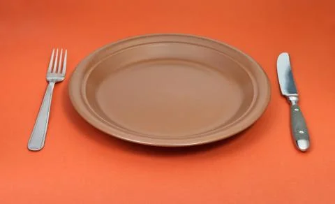 Empty ceramic plate with fork and knife on red Stock Photos