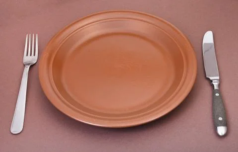 Empty ceramic plate with fork and knife on brown Stock Photos