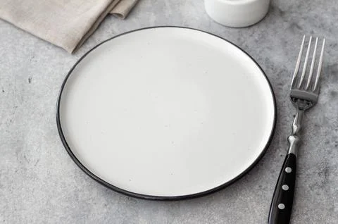 Empty ceramic plate with fork on gray stone table, minimal rustic table set.. Foto stock