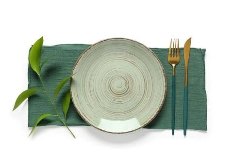 Empty ceramic plate with green napkin, gold cutlery, and a fresh plant branch Stock Photos